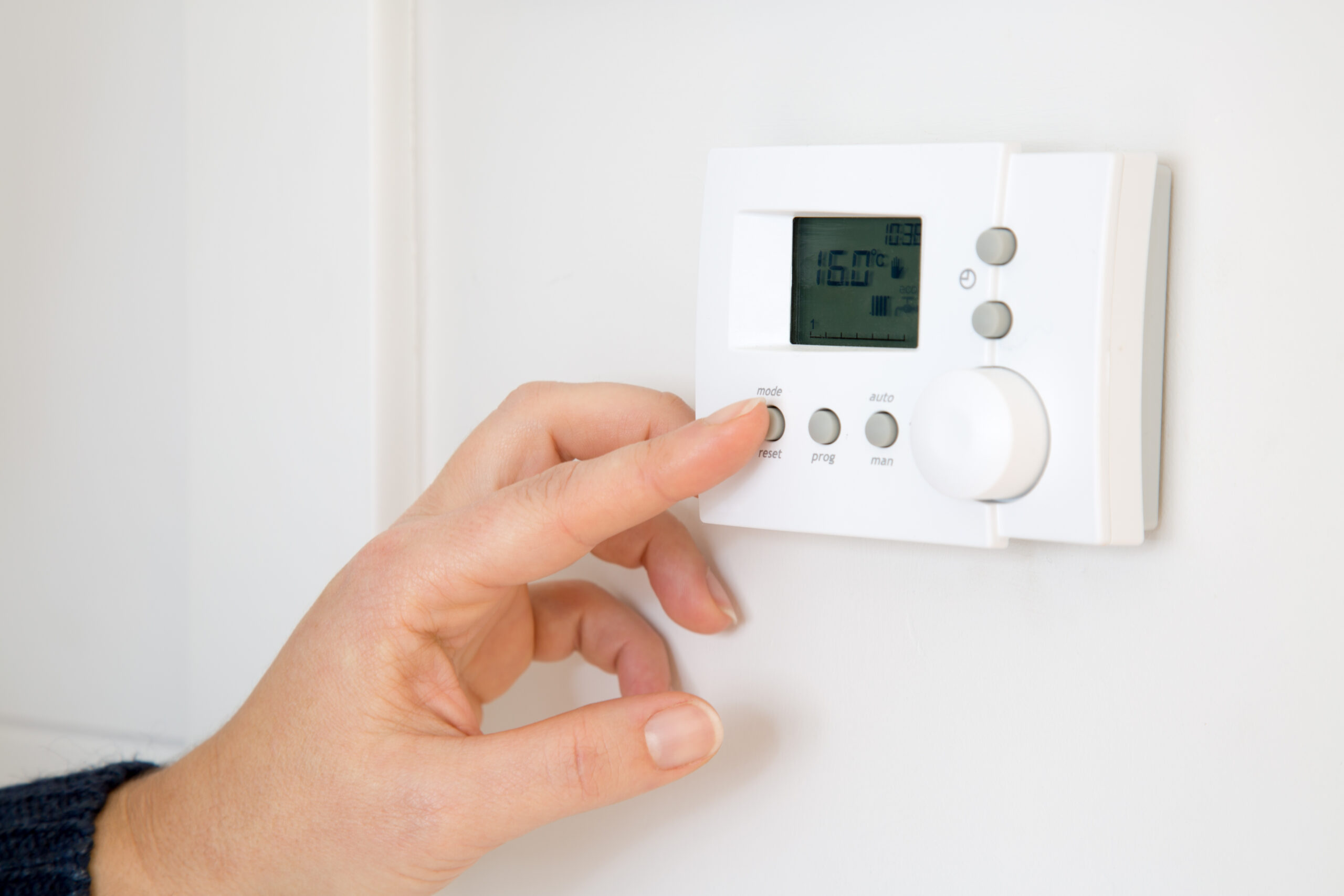 Woman adjusting digital central heating thermostat at home